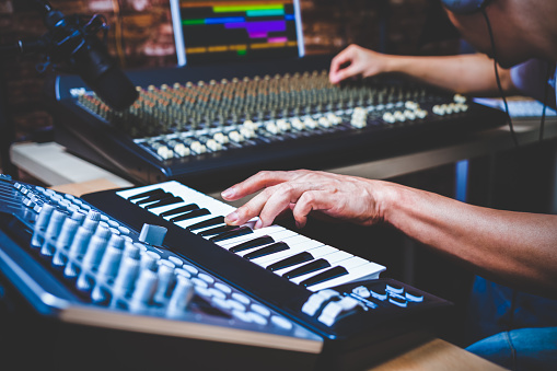 male musician playing midi keyboard synthesizer in recording studio, focus on hands