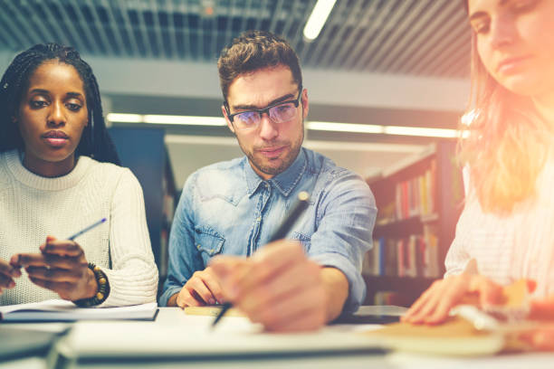 istock Handsome confident male leader of working group signing documentation feeling determination in decision, student writing answer in testings sitting on lesson near female colleagues in classroom 905130492