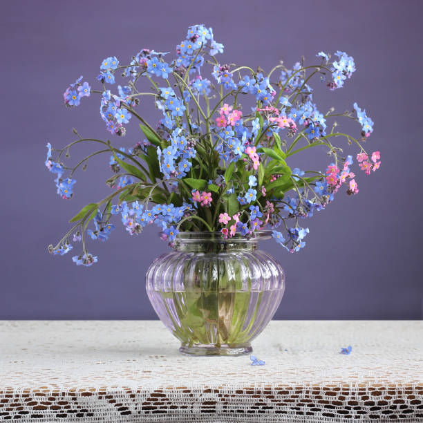 istock Forget-me-nots (Myosotis) in a vase on purple background. 905138916