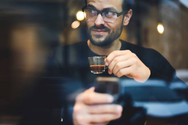 Cropped image of smart handsome businessman with stylish spectacles holding digital tablet and glass with coffe in hand. Close up young man using modern device and using free internet connection