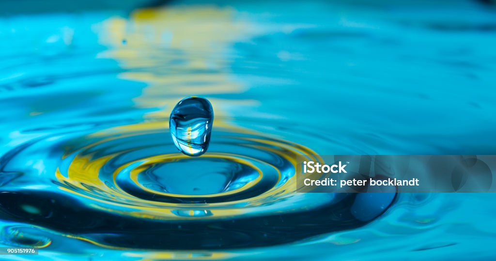 water drop in a glass of water water drop splash in a glass blue colored Water Stock Photo