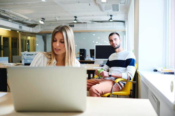 istock Portrait of male skilled architect on background having spare time during work break with cup of coffee while his female coworker planning design for modern construction via laptop computer and  wifi 905157330