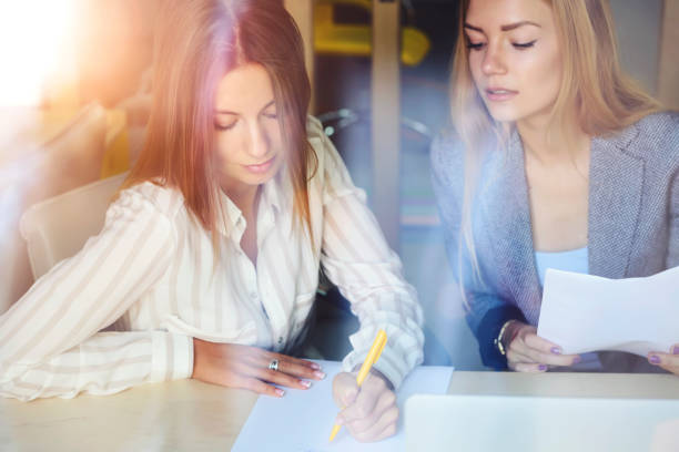 istock Young female student writing down dictation with pen and paper while having individual lesson with foreign language talented teacher consultation about upcoming testing quality control in classroom 905163010