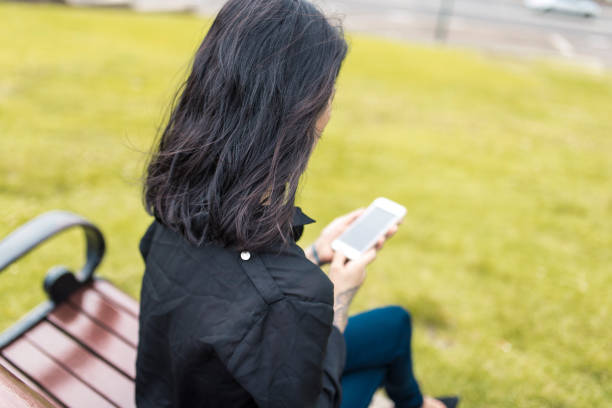 mujer asiática utilizando teléfonos inteligentes en el parque - tattoo women back rear view fotografías e imágenes de stock