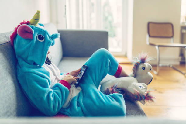 niña en traje del unicornio con el móvil en el sofá - ropa de escuela perezosa fotografías e imágenes de stock