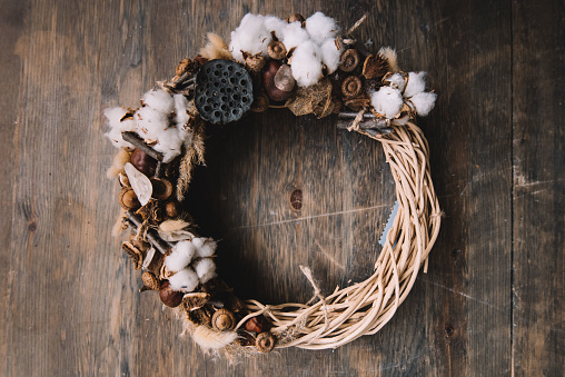 Beautiful festive hand-crafted wooden wreath decorated with cotton and other organic pieces, rustic old wooden table background, top view