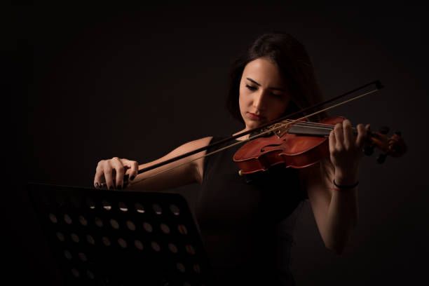 hermosa mujer joven tocando un violín sobre fondo negro - violin women violinist music fotografías e imágenes de stock