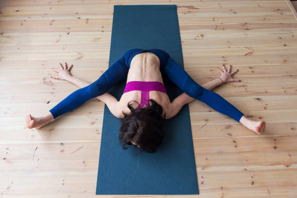 istock Top view of female yogi doing advanced kurmasana tortoise pose on mat indoors while practicing yoga 905203944