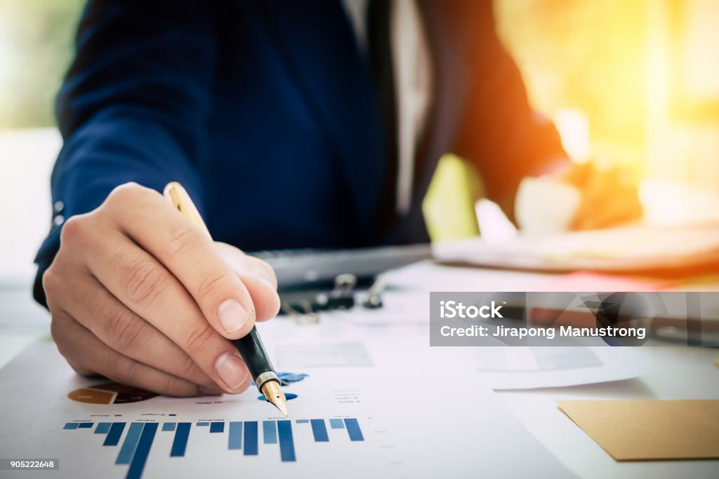 Businessman pen pointing graph chart in this mounth and using la Businessman pen pointing graph chart in this month and using laptop computer, calculator for  Plans to improve quality next month. Tax Stock Photo