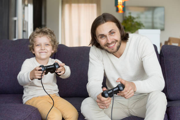istock Father and son holding joysticks playing video games at home 905222696