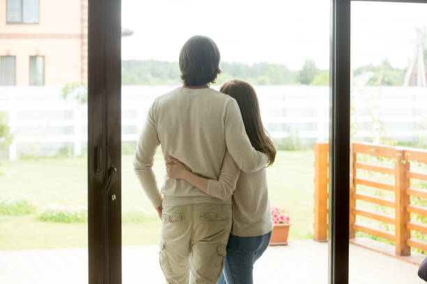 istock Couple standing at home, embracing looking outside, rear view 905222794