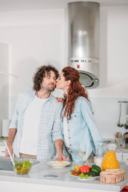 istock girlfriend kissing happy boyfriend at kitchen 905230070