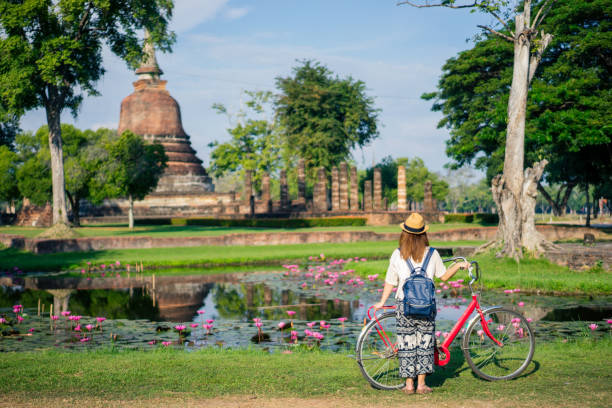 junge frau reisenden reisen mit dem fahrrad in tempel wat mahathat in sukhothai historical park enthält die ruinen des alten sukhothai, thailand, unesco-weltkulturerbe. - bangkok thailand asia temple stock-fotos und bilder