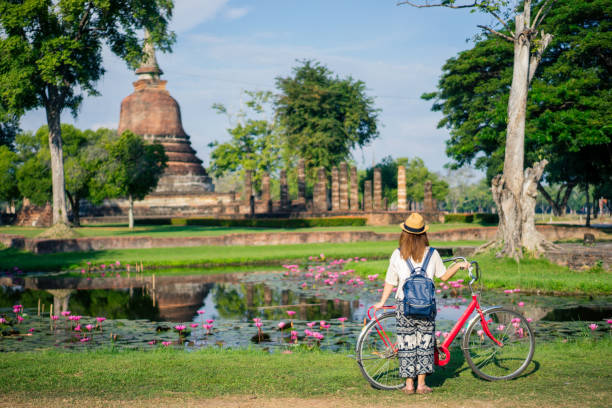 voyageur de jeune femme voyageant à vélo dans le temple de wat mahathat dans le parc historique de sukhothai contient les ruines de la vieille sukhothai, thaïlande, mondial de l’unesco patrimoine de l’humanité. - buddha ancient asia asian culture photos et images de collection