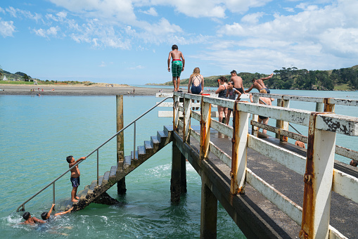 RAGLAN NEW ZEALAND - JANUARY 14, 2018; Summer fun in Raglan mostly local Maori boys jumping from the small wharf in small New Zealand town on North Island's West Coast.