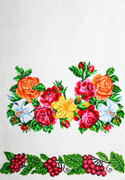 top view of the cross stitch process, white canvas Aida 14 counts, it has beautiful pink flowers, a needle, floss threads, vintage little needlework scissors and lace ribbon