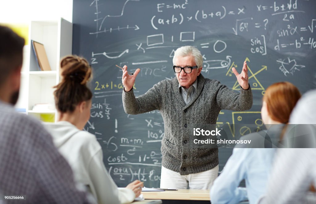 Teacher by blackboard Excited teacher looking at group of students while explaining his subject Teacher Stock Photo