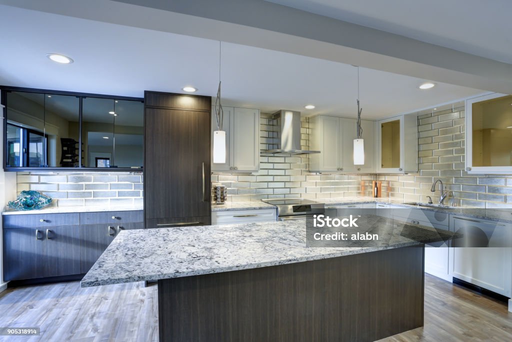Modern kitchen room in a condo home Well appointed kitchen features a large kitchen island, gray quartzite countertops,  silver backsplash and white shaker cabinets . Quartzite Stock Photo