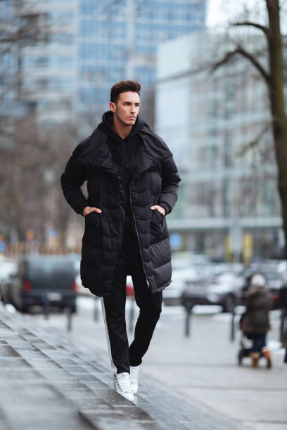 stylish man wolk on the street. winter cold outfit. big jacket with white sneakers. blured background street. profecional model photo. - wolk imagens e fotografias de stock