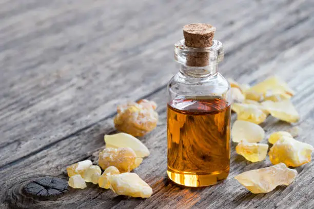 A bottle of frankincense essential oil with frankincense resin on a wooden table with copy space