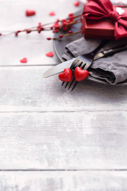 istock Festive table setting for Valentine's Day with fork, knife and hearts on a white wooden table. Space for text. Top view. 905333398