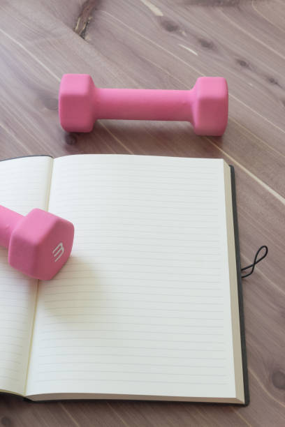 istock Two pink hand weights with open, blank journal, on a wood table top, copy space, neutral colors 905343152
