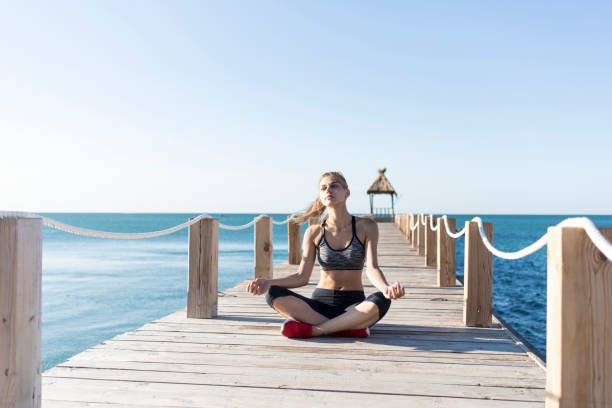 istock Young woman sitting on pier and practicing 905352452