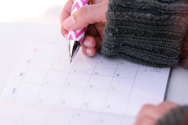 Closeup of a woman's hands as she makes a note in her calendar.