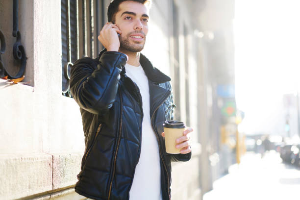 istock Thoughtful bearded tourist looking away while communicating via smartphone in roaming standing in sunshine street.Handsome pensive male talking on cellular and holding tasty coffee while strolling 905358486