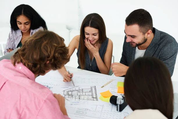 istock Crew of skilled architects having fun during informal meeting working on new successful project drawing map on new construction edifice finding solution of graphic problems sitting in modern office 905358534