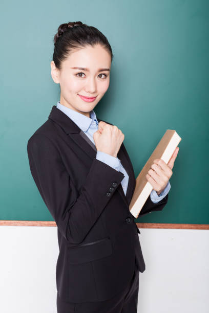 istock female teacher holding book front of blackboard 905361766