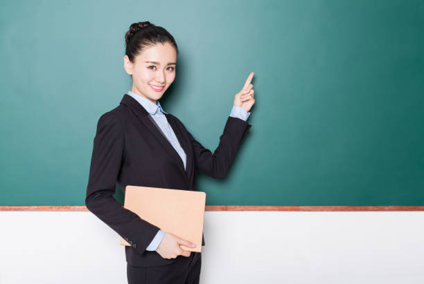 istock female teacher holding book front of blackboard 905361796