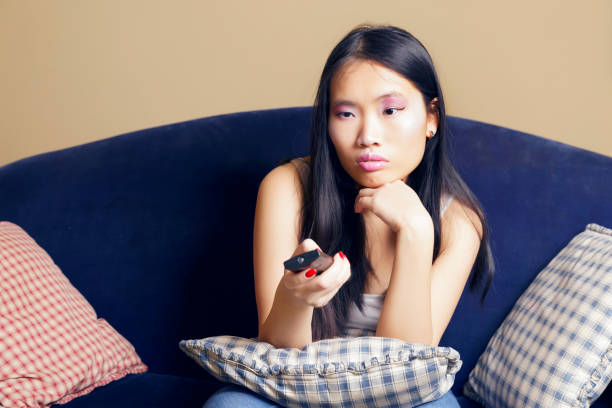 istock Bored asian girl sitting on a sofa, watching tv. 905364238