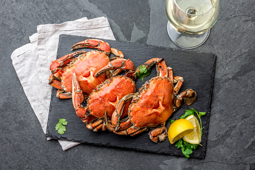 Cooked crabs on black plate served with white wine, black slate background, top view.