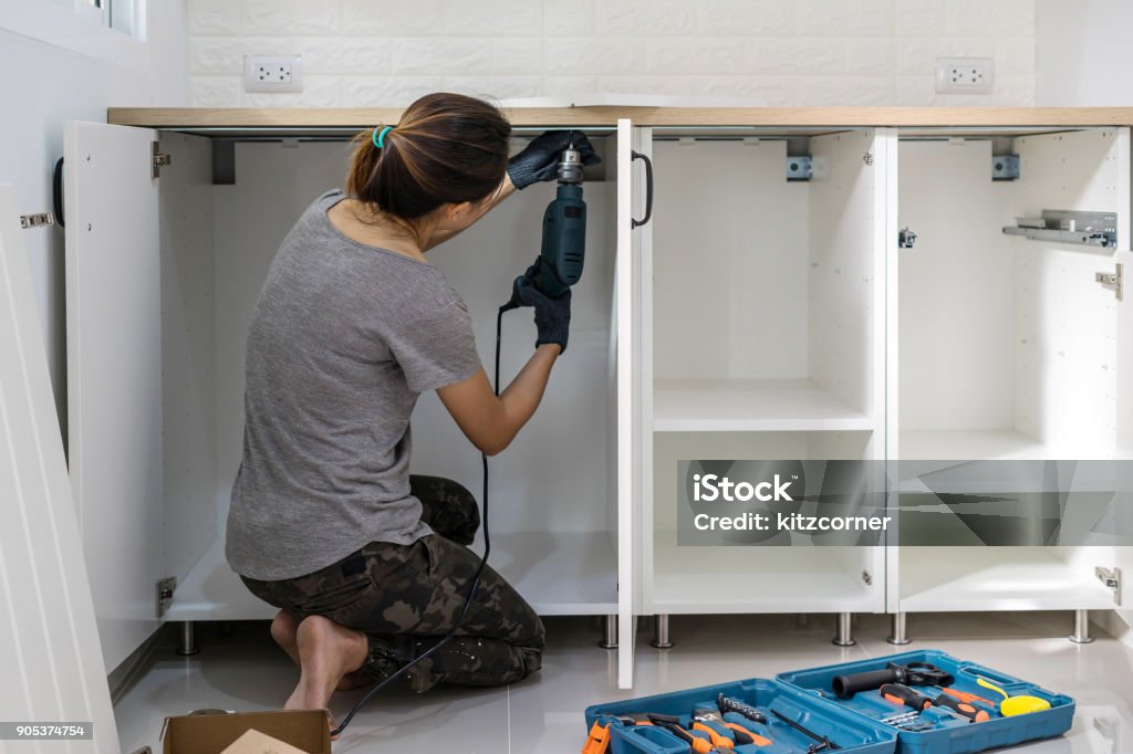 Young woman using electric screwdriver to installation Young woman using electric screwdriver to installation kitchen furniture, DIY concept Kitchen Stock Photo