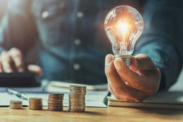 istock business man hand holding lightbulb with using calculator to calculate and money stack. idea saving energy and accounting finance in office concept 905376604