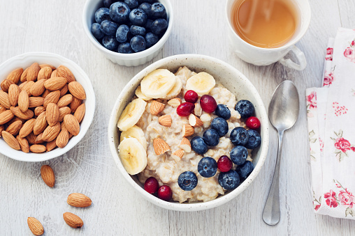 Oatmeal porridge with berries, nuts and cup of green tea on gray table. Top view. Dieting, healthy eating concept