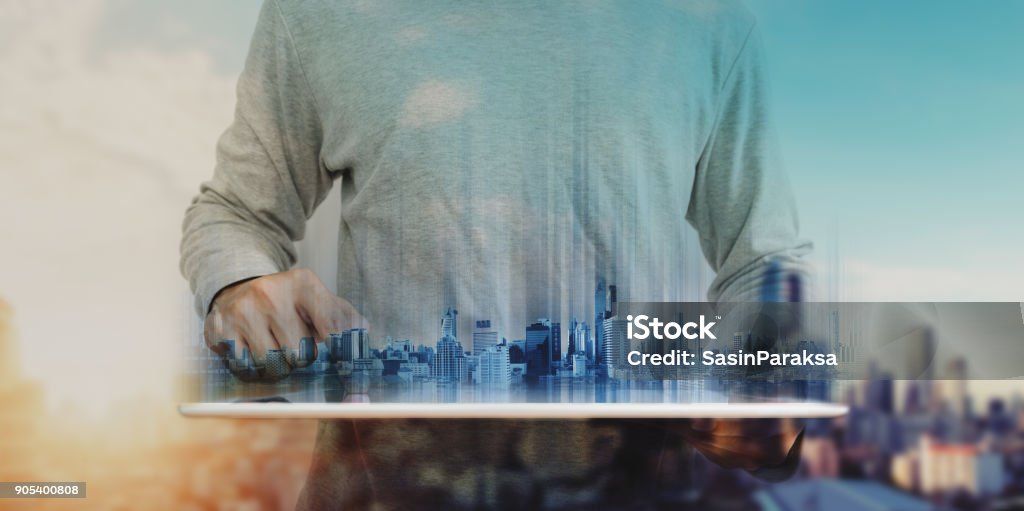 a man working on digital tablet, with Hologram futuristic modern buildings. City sunrise background Construction Industry Stock Photo