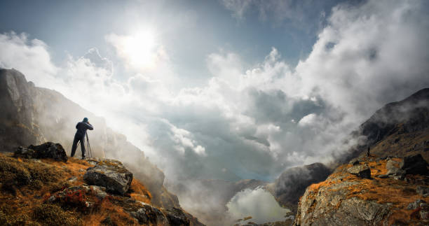 photographer traveler with camera taking photo of mountains standin on top of a mountain and enjoying photograph - nature photographer imagens e fotografias de stock