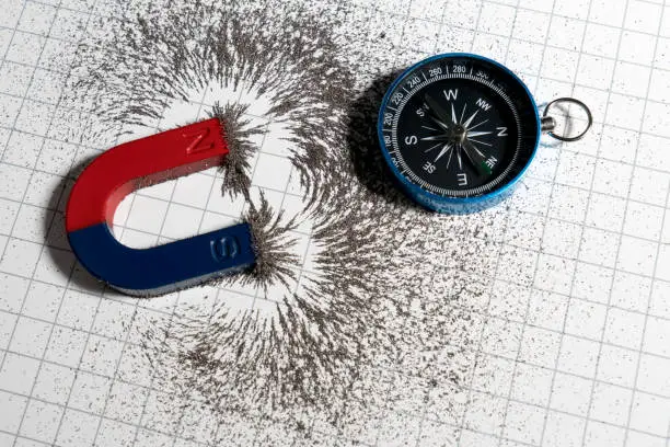 Red and blue horseshoe magnet or physics magnetic and compass with iron powder magnetic field on white paper graph background. Scientific experiment in science class in school.