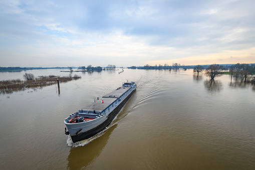 Flooding in the overflow area of the river IJssel in  The Netherlands with a barge freight ship passing in the morning