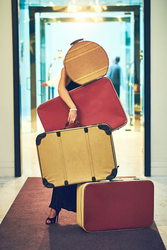 Shot of an unrecognizable young woman carrying a whole bunch of luggage while trying to walk down the lobby of a hotel