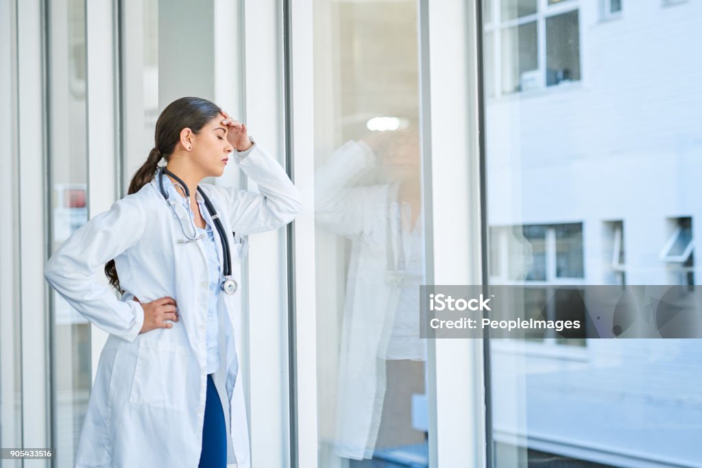 She's had to make some tough decisions today Shot of a young female doctor looking stressed out while standing at a window in a hospital Doctor Stock Photo