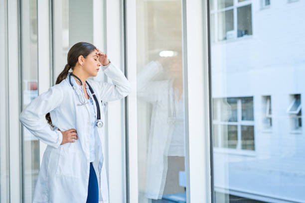 She's had to make some tough decisions today Shot of a young female doctor looking stressed out while standing at a window in a hospital Tensed stock pictures, royalty-free photos & images