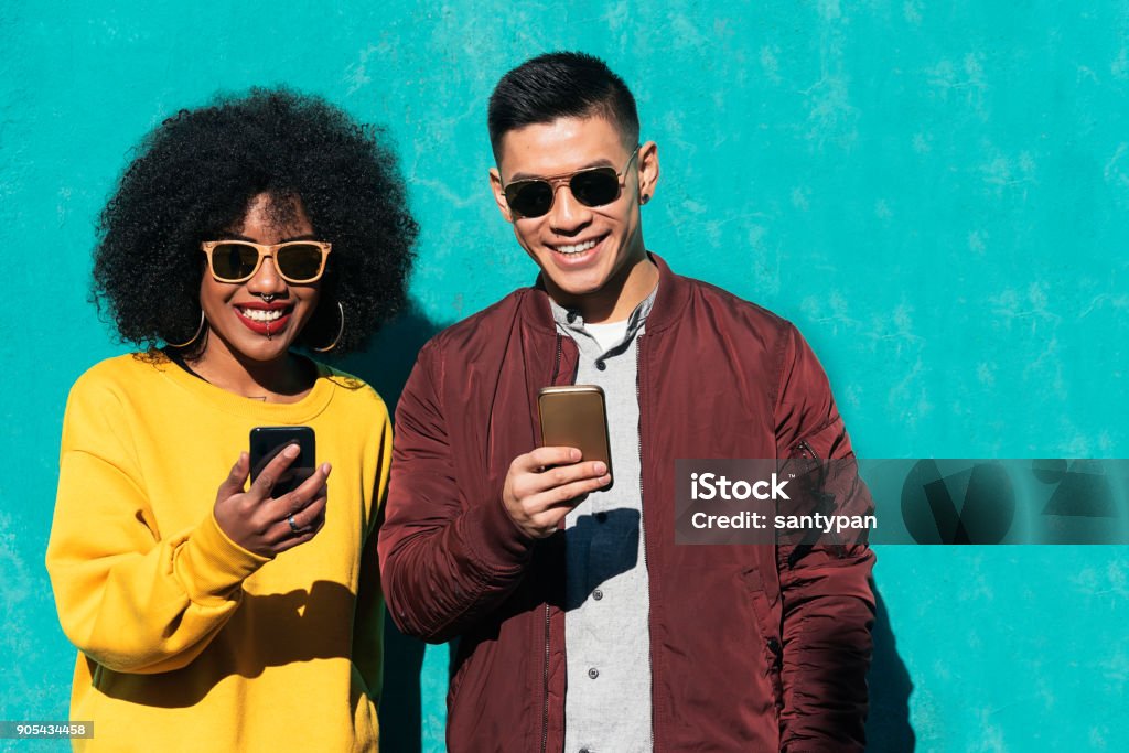 Two happy friends using the mobile in the street. Two happy friends using the mobile in the street. Friendship concept. Friendship Stock Photo