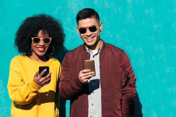 два счастливых друга, использующих мобильный телефон на улице. - teenager beautiful female men стоковые фото и изображения