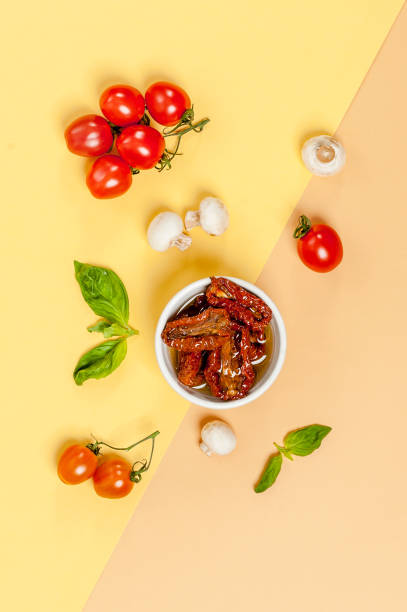 Sun dried tomatoes, champignon mushrooms, fresh tomatoes and basil leaves are ingredients on a yellow-orange pastel background. stock photo