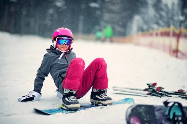 Portrait of girl in ski outfit learning to snowboard. 
