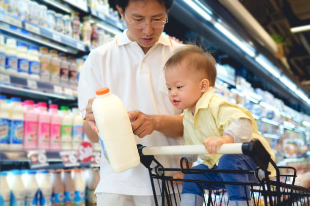 asiatischen vater & niedlich, die kleine 18 monate/1 jahr altes kleinkind jungen kind milch produktauswahl im lebensmittelgeschäft, papa milch ernährung, die fakten mit kind sitzen gelesen in den warenkorb - baby pointing child showing stock-fotos und bilder