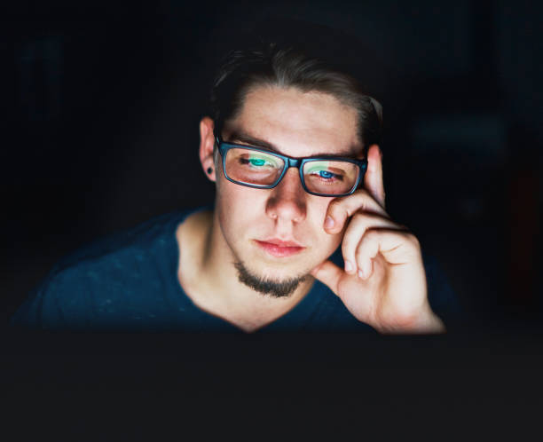 コンピューターのモニターに暗く見つめていた若い男が座っています。 - teenager dark pensive emotional stress ストックフォトと画像